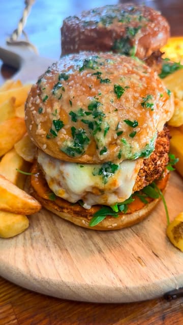 A short, instructional video demonstrating how to assemble a chicken parmesan burger at home using pre-made chicken patties, breadcrumbs, tomato sauce, mozzarella, and garlic butter.