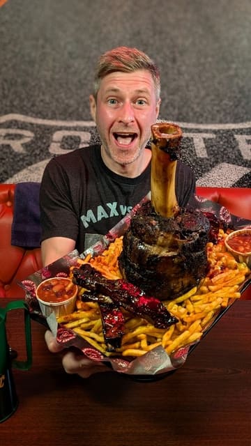A food challenge video featuring the 'Thor's Hammer' at Burnout Barbecue in Oxford. The creator presents the massive platter, which includes a 6lb beef shank, Cajun fries, mac and cheese, smoked pork ribs, and BBQ beans, all served with a jug of gravy. The video highlights the scale of the challenge and the components of the meal.