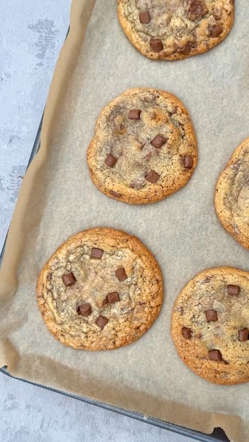 A short, satisfying video showing the process of making cookies, from mixing the dough with chocolate chips and candies to scooping them onto a baking tray and showing the final baked result.