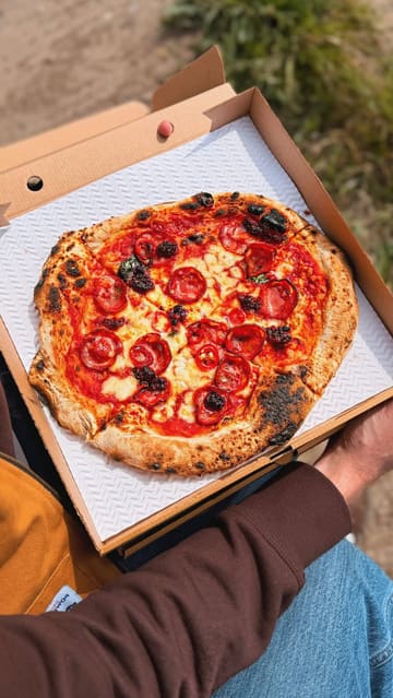 A couple visits a home-based pizza pop-up called Backyard Dough Co in Barry, Wales. The video documents the pizza-making process, the creator's setup, and the final product, which they enjoy by the sea.