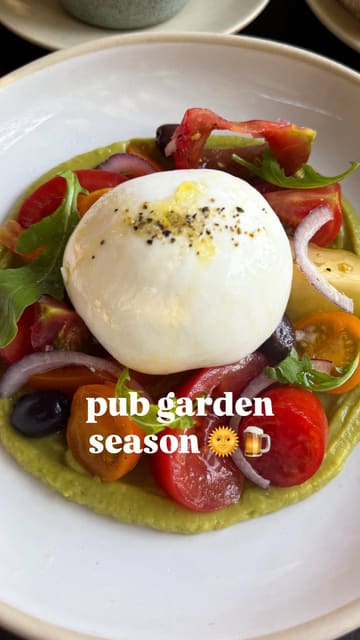 A short, fast-paced montage showcasing a variety of dishes from a pub's summer menu, including wings, a cheese soufflé, scallops, a tomato and burrata salad, and a basque cheesecake, set against the backdrop of the pub's garden and covered seating area.