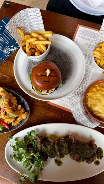 A promotional video for All Bar One's 'Bottomless Fridays' offer, featuring a variety of dishes including a burger, steak, calamari, and mac and cheese, alongside cocktails and prosecco.