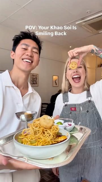 A couple showcases a playful 'Khao Soi' dish featuring smiley-face potato snacks at a restaurant called Plants of Roslin, demonstrating the assembly of the meal.