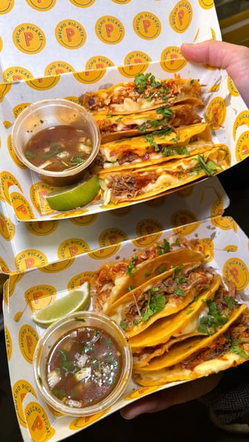 A short, high-energy promotional video for Mucho Picante, a street food vendor specializing in birria tacos. The video features quick cuts of the food truck, close-ups of the tacos being dipped in consommé, and a display of the menu and drink options.
