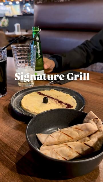A short montage showcasing a meal at a grill restaurant, featuring shots of hummus, a steak, a mixed grill platter, and fries, along with a brief glimpse of the restaurant interior.