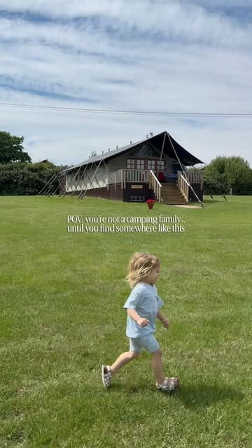 A short, bright video clip featuring a child running through a grassy field towards a large safari-style glamping tent. The video uses a 'POV' text overlay to frame the experience as a family-friendly getaway, highlighting the appeal of the accommodation for those who aren't typical campers.