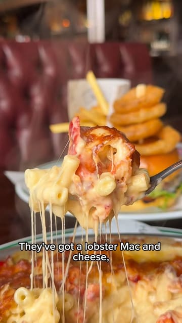 A lively food review vlog featuring two presenters visiting Wavertree Town Hall. They sample a variety of pub-style dishes including a Scotch egg, salt and pepper chicken wings, a sausage roll, gammon steak, a burger, lobster mac and cheese, and sticky toffee pudding, providing commentary on the quality and value of the food.