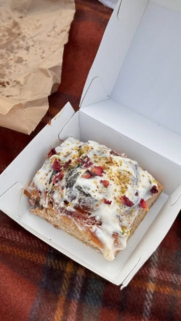 A creator visits Bunhead Bakery to showcase their vegan-friendly options, highlighting various buns, focaccia, and drinks while enjoying them in a park.
