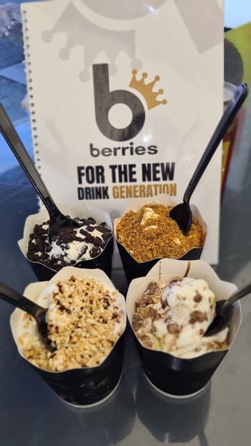 A short, visually-focused montage showing the preparation of soft-serve ice cream desserts at Berries King of Shakes, featuring various toppings like sauces and crushed biscuits.