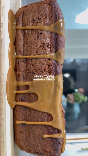A high-quality, close-up food video demonstrating the finishing touches of a sticky toffee banana bread, featuring slow-motion pours of toffee sauce and cream, followed by slicing and stacking.
