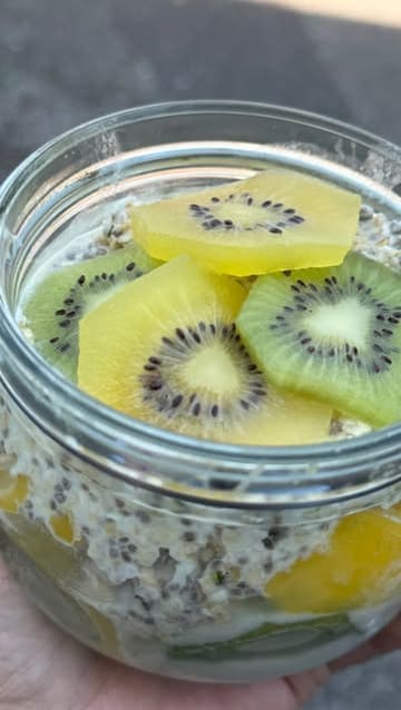 A recipe tutorial demonstrating how to prepare overnight oats using cacao fruit pulp, rolled oats, seeds, coconut, and fresh fruit. The video is a top-down, instructional edit focusing on the preparation process.