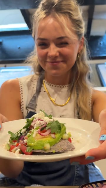 The video follows two creators attending a Mexican street food cooking class at a cookery school. It documents the process of making tlacoyos, from shaping the corn dough to topping the finished dish with avocado, salsa, and cheese. The tone is upbeat and educational, highlighting the hands-on nature of the experience.