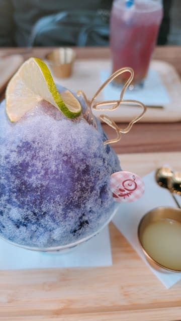 A short-form video showcasing a new menu at a dessert cafe, featuring close-up shots of bingsu, tofu pudding, sandwiches, and a fried snack platter. The video uses text overlays to describe the items and highlights the visual appeal of the food, particularly a color-changing bingsu.
