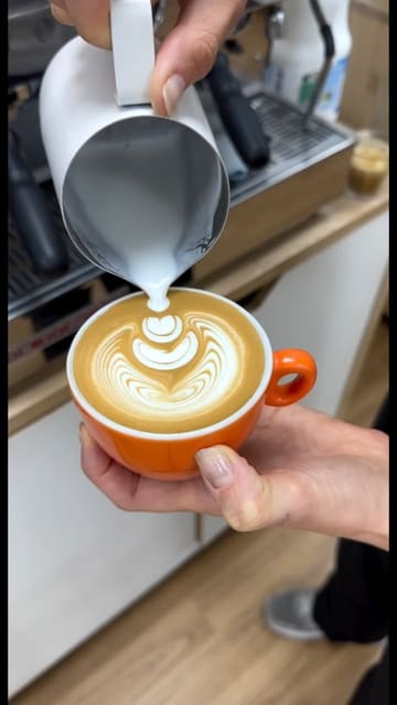 A close-up, high-quality video focusing on the process of pouring latte art into a bright orange coffee cup. The video captures the precision of the pour, resulting in a clean, professional design.