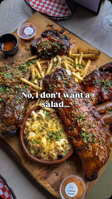 A polished, slow-motion montage focusing on a large, indulgent BBQ meat platter. The video uses high-quality close-ups to highlight the texture of the ribs, brisket, and sides, effectively selling the food without showing the venue or a creator.