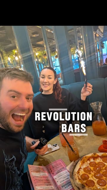 A fast-paced vlog featuring two creators visiting Revolution Brighton. The video highlights the venue's interior, a 33% off food promotion via their app, a pepperoni pizza, large cocktail pitchers, and a variety of flavoured shots, capturing a fun and social atmosphere.