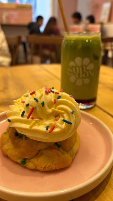 A short, handheld video showcasing a visit to a vegan cafe called Sunday. The video features shots of the cafe exterior, a table spread of various drinks and cookies, a close-up of a cookie being broken, and a shot of a dog inside the venue.