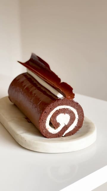 A creator demonstrates the process of making a chocolate swiss roll while sharing a personal story about the publication of their baking book.