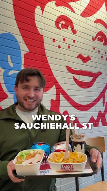 A creator visits a newly opened Wendy's in Glasgow, providing a review of various menu items including a spicy chicken Caesar salad, halloumi sticks, cheesy fries, chicken nuggets, a chicken burger, a beef burger, a Kit Kat Frosty, and mini cinnamon donuts.