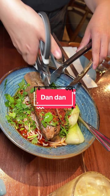 The creator visits Dan Dan, a Chinese restaurant in London, providing a review of their experience. The video features close-ups of various dishes including beef ribs noodles, spring rolls, dim sum, squid, soup, and cucumber salad, alongside shots of the restaurant's interior and the creator enjoying the food.