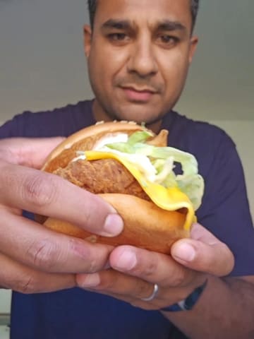 A short, casual video demonstrating a 'samosa burger' hack using a McDonald's burger and a samosa, presented as a fun fusion idea for World Samosa Day.