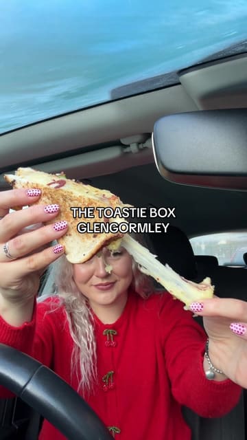 A food review video featuring a creator trying various toasties and loaded hash browns from a food truck called Toastie Box in Glengormley. The creator provides a breakdown of the menu items, including the hot honey chicken toastie, the treatso chorizo toastie, and a stacked toastie, while sharing her thoughts on the flavours and portion sizes.