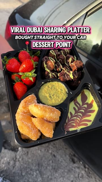 A short, punchy video showcasing a 'viral Dubai sharing platter' from Dessert Point, featuring close-up shots of dipping strawberries, brownies, and fried dough into sauces while inside a car.
