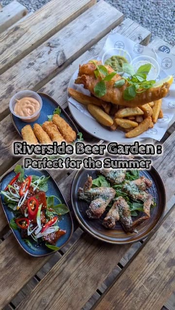 A promotional reel for 'The Moorings', a riverside pub and kitchen. The video features a montage of the venue's exterior, interior, beer garden, and riverside seating pods, interspersed with close-up shots of various dishes including fish and chips, chicken wings, halloumi sticks, pork belly, and desserts.