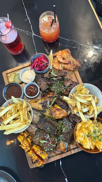 A food review video showcasing a BBQ platter, tacos, and cocktails at Smoky Boys in Milton Keynes. The video features close-up shots of the food, including ribs, grilled prawns, corn, and mac & cheese, as well as a brief look at the menu and venue interior.