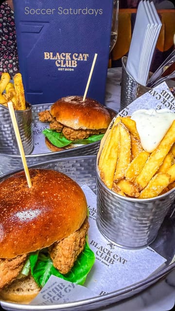 The video showcases the 'Soccer Saturday' experience at Black Cat Club in Liverpool, highlighting the bottomless drink offer, food options like burgers and pizzas, and competitive socialising activities such as shuffleboard and darts.