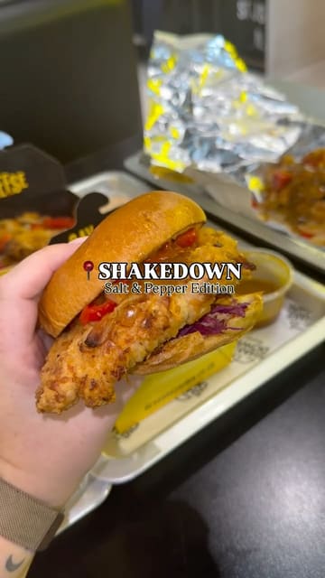 A short, casual video showcasing the 'Salt & Pepper' limited edition menu at Shakedown, featuring a chicken burger, spice bag, and chicken wings. The video includes close-up shots of the food, the menu, and the venue's interior, with a focus on the curry sauce pairing.