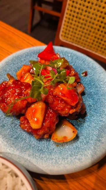 A short, handheld-style video review of YiQi Lah!, a Southeast Asian street food canteen in London's Chinatown. The video features shots of the restaurant's exterior and interior, followed by a montage of various dishes including chicken wings, prawns, and rice, highlighting the vibrant and spicy nature of the food.