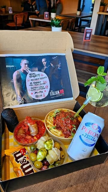 A promotional reel featuring a themed 'Mom's Spaghetti' munch box, showcasing various Italian-inspired street food items including a meatball-stuffed pasta dish, a microphone-shaped croquette, and fried sausage. The video uses close-up shots to highlight the textures and interactive elements of the food, such as injecting basil oil.