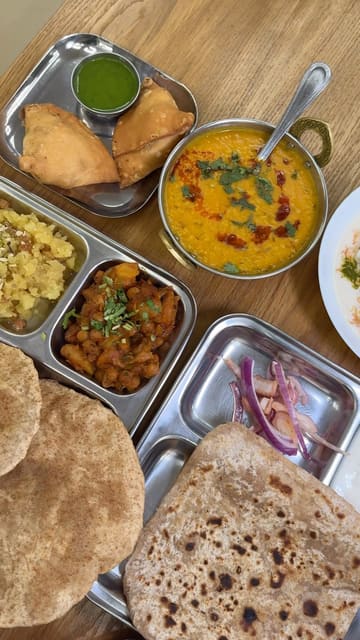 A montage of close-up shots featuring various Indian dishes including samosas, papri chaat, tadka daal, and paratha at Anand Sweets. The video focuses heavily on the texture and preparation of the food, with minimal shots of the venue itself.