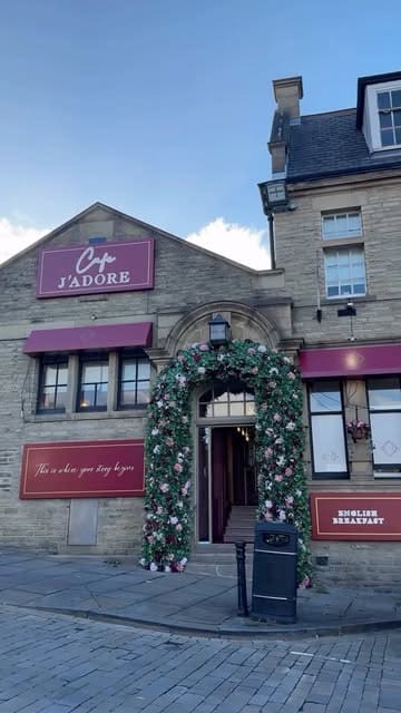 A promotional montage for Cafe J'adore in Batley, featuring shots of the venue's floral-themed interior, cocktails, tacos, a chicken dish, and dessert pancakes.
