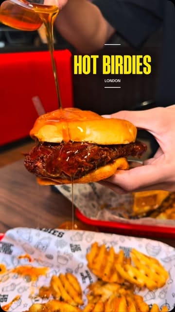 A fast-paced, music-driven montage showcasing various Nashville-style hot chicken burgers, sandwiches, waffle fries, and desserts at Hot Birdies in London. The video focuses on close-up shots of food preparation and textures, such as cheese pulls and sauce drizzles, to entice viewers.