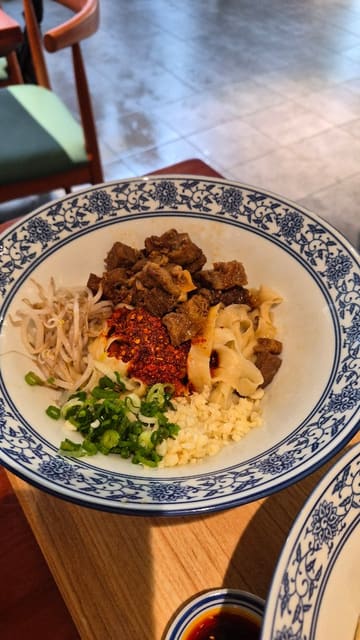 A short-form video review of JWD Hand-Pulled Noodle Bar in Cambridge, featuring shots of the ordering kiosk, the open kitchen, and various noodle dishes and a Chinese burger (rougamo).