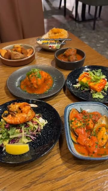 A promotional video for La Fiesta in Leeds, highlighting their all-you-can-eat Mediterranean small plates concept. The video features a montage of various dishes, the salad and charcuterie buffet, the ordering tablet, and cocktails, set to music with text overlays describing the experience.
