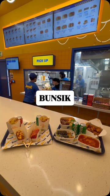 A fast-paced promotional video showcasing a variety of Korean street food dishes at a Bunsik location in the Trafford Centre, featuring corn dogs, kimbap, tteokbokki, and fried chicken.