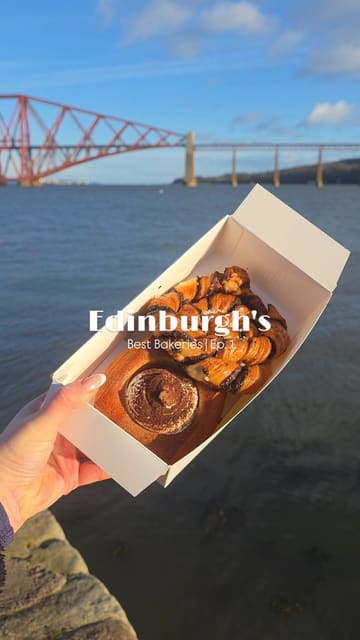 A short, engaging video review of Dune Bakery in South Queensferry, Edinburgh. The creator showcases the bakery's offerings, including specific pastries like the Chocolate Babka and Dauphinoise Potato Special, while highlighting the scenic location near the Forth Bridge. The video features a mix of shots of the queue, the display case, the food, and the creator interacting with their dog.