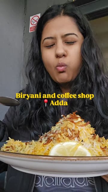 A short vlog-style video featuring a visit to 'Adda', showcasing the interior and outdoor seating areas, followed by close-ups of pink tea, biryani, and chicken momos being eaten by the creator.