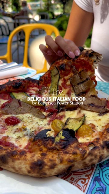 A short, handheld-style video showcasing Italian dishes, specifically zucchini fries and a vegetable pizza, at Tozi restaurant near Battersea Power Station.