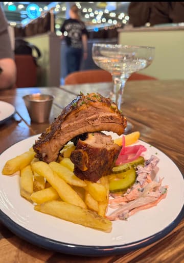 A food review video showcasing the menu at Bear Bones BBQ Co, featuring close-ups of ribs, brisket, turkey, and mac and cheese, along with shots of the venue interior.