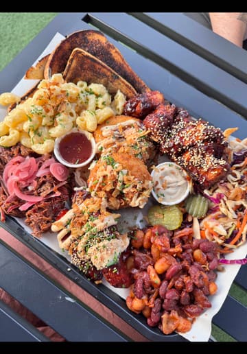 A promotional video for Fat Jack's Shack in Chichester, featuring a variety of American BBQ dishes including ribs, wings, and mac and cheese, set in an outdoor courtyard venue.