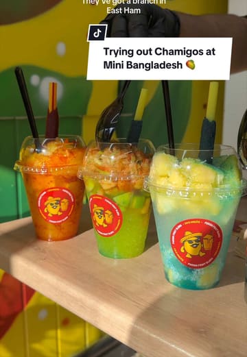 The video provides a tour of the Mini Bangladesh area in Green Street, London, highlighting the variety of shops and specifically focusing on a new dessert spot called Chamigos. It features close-up shots of the preparation of various mango-based slushies and desserts, accompanied by a voiceover review.