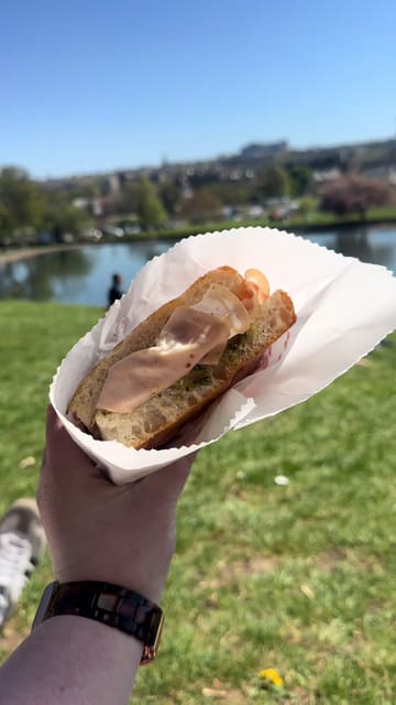 A short, energetic reel showcasing a visit to Mootz in Stockbridge, Edinburgh. The video features a handheld shot of a sandwich being enjoyed in a nearby park, followed by a quick tour of the venue's interior, including the menu board, decor, and a polaroid wall.