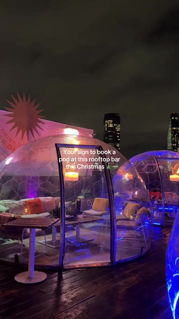 A promotional video showcasing a rooftop bar decorated for Christmas, featuring private dining pods, cocktails, and various food dishes.