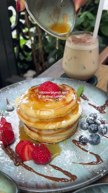 A short, aesthetic montage showcasing a brunch spot in West London, featuring close-ups of pancakes, avocado toast, pasta, and iced coffee, alongside shots of the outdoor seating area.