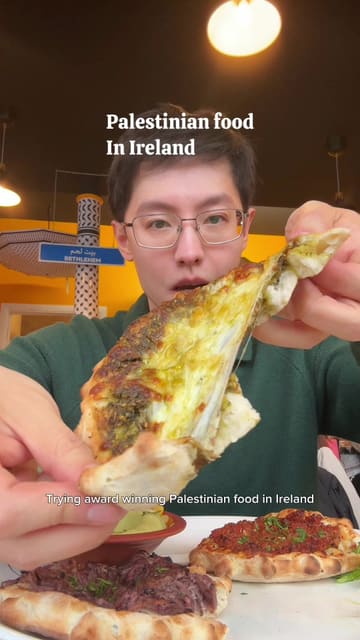 A creator reviews Palestinian food at Izz Cafe in Cork, Ireland, highlighting various manaeesh (flatbreads) and stuffed vine leaves. The video features close-up shots of the food, including a cheese pull, and provides descriptive commentary on the flavors and ingredients.