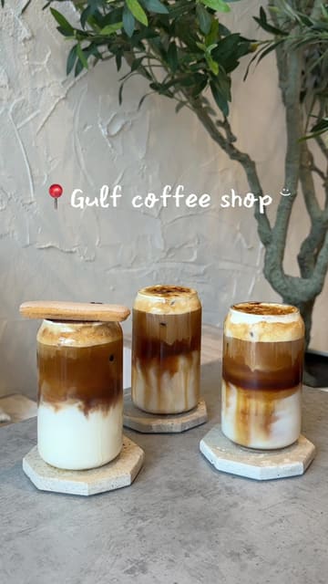 A review of a coffee shop called Gulf in Manchester, highlighting their specialty iced lattes including Tiramisu, Creme Brulee, and Saffron flavors. The video features the creator visiting the venue, showing the menu, the aesthetic interior, and tasting the drinks.